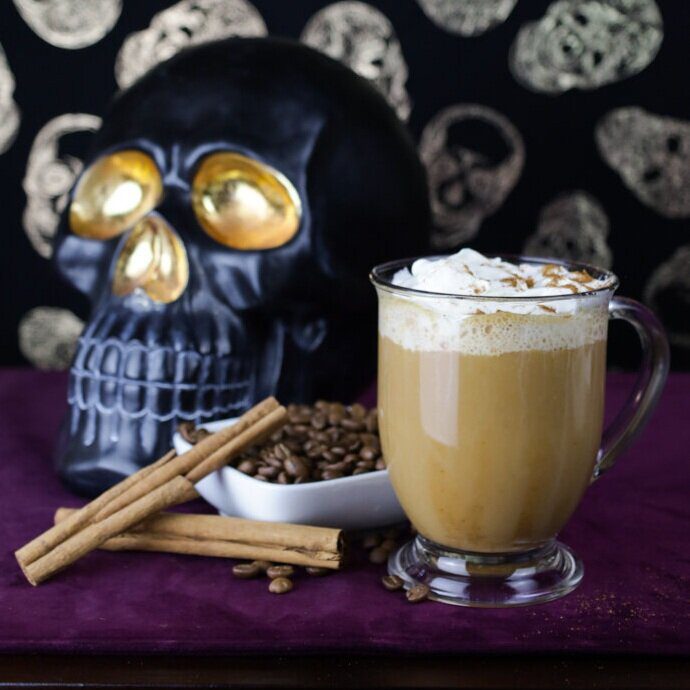 A spooky halloween black and gold skull next to a fresh brewed cup of coffee.