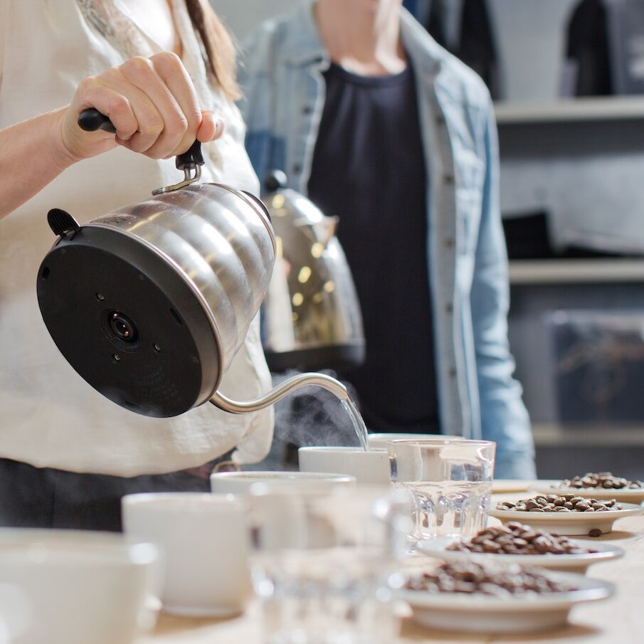 Coffee taster pouring hot water into cup of coffee