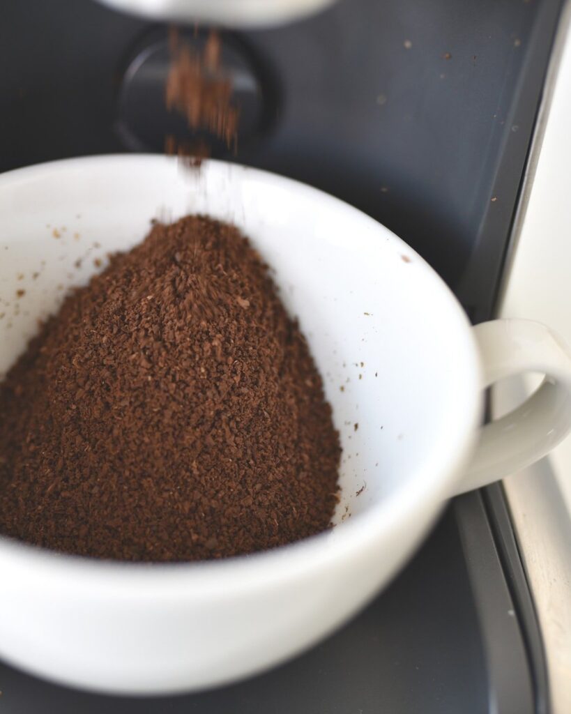 Fresh gourmet/specialty coffee grounds dispensing from an automatic burr coffee grinder.