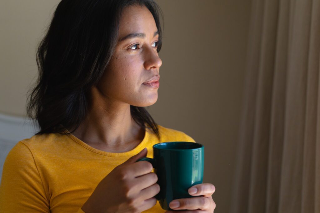 Young african american woman thinking while holding coffee mug at home