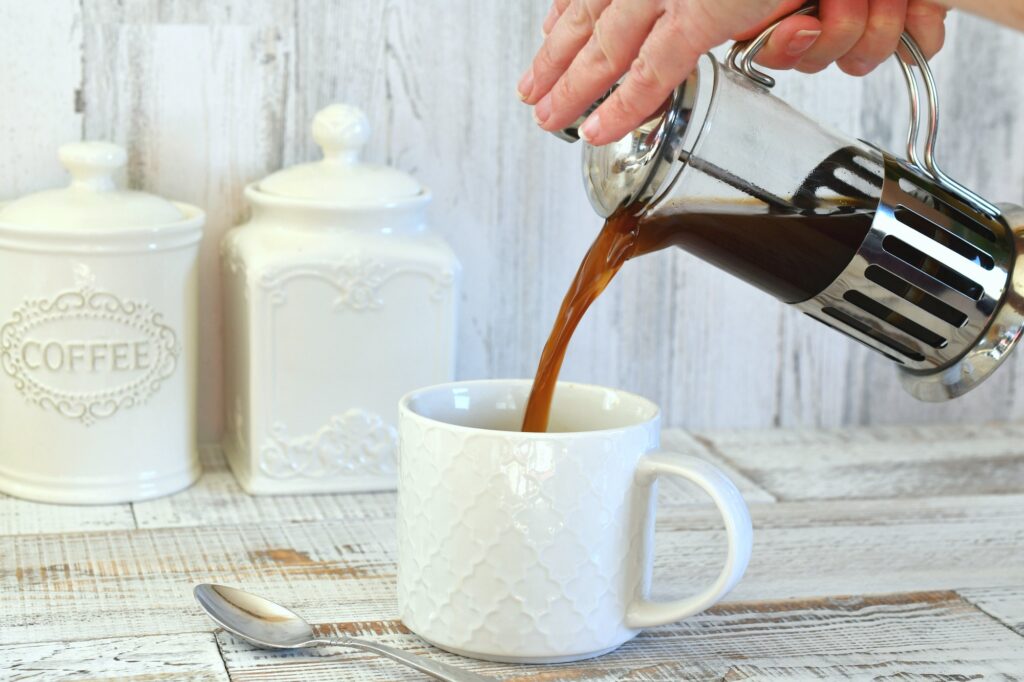 Pouring coffee from a French press coffee maker into a white mug.