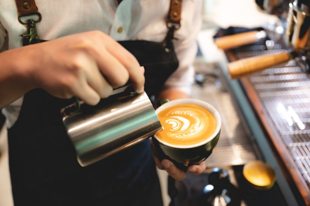 professional barista making latte art from coffee and milk, hand holding a cup of latte