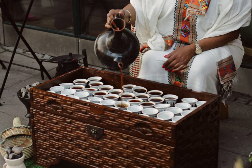 Ethiopian woman wearing traditional clothing and serving coffee in small cups. - "The Black History of Coffee"